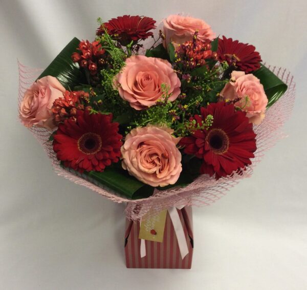 This stunning handtied is a mix of classic red and peach colours, including roses, gerberas and thaspelli greens. This is perfect for all occasions, including romantic, anniversary or birthdays.